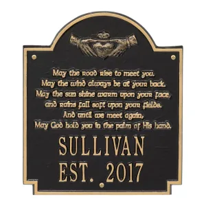 Black and gold plaque featuring an inscription and decorative elements, including a pair of hands holding a heart.
