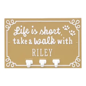 Wall-mounted plaque with the phrase 'Life is short, take a walk with RILEY' and three hooks for hanging items.