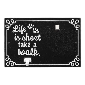 Black plaque with white lettering that reads 'Life is short take a walk' and paw prints.
