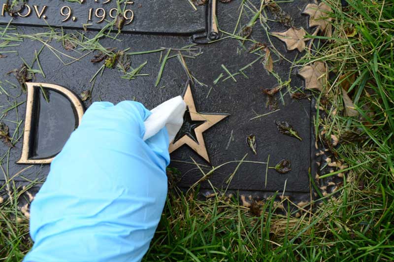 Cleaning a bronze grave marker with a gloved hand